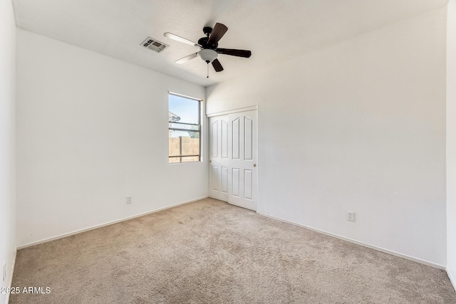 empty room featuring light carpet, visible vents, baseboards, and ceiling fan
