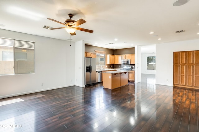 kitchen with open floor plan, a center island, appliances with stainless steel finishes, and ceiling fan