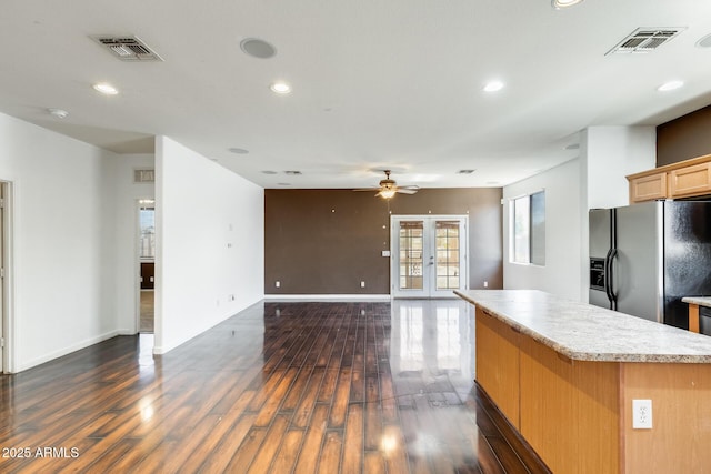 kitchen with dark wood-type flooring, a center island, black refrigerator with ice dispenser, and visible vents