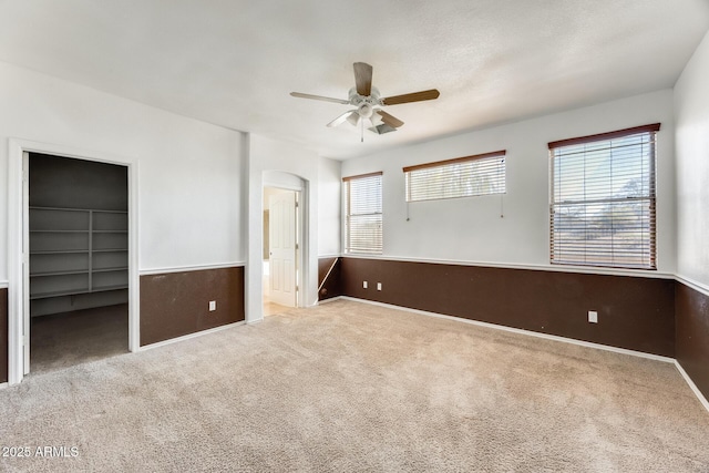 unfurnished bedroom featuring ensuite bathroom, carpet floors, a walk in closet, ceiling fan, and arched walkways