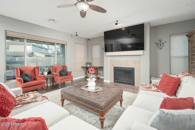 living room with wood finished floors, visible vents, baseboards, ceiling fan, and a tiled fireplace