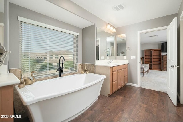 bathroom with visible vents, connected bathroom, a freestanding bath, wood finished floors, and vanity