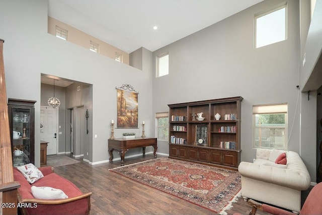 living area with a high ceiling, baseboards, dark wood-style flooring, and a chandelier