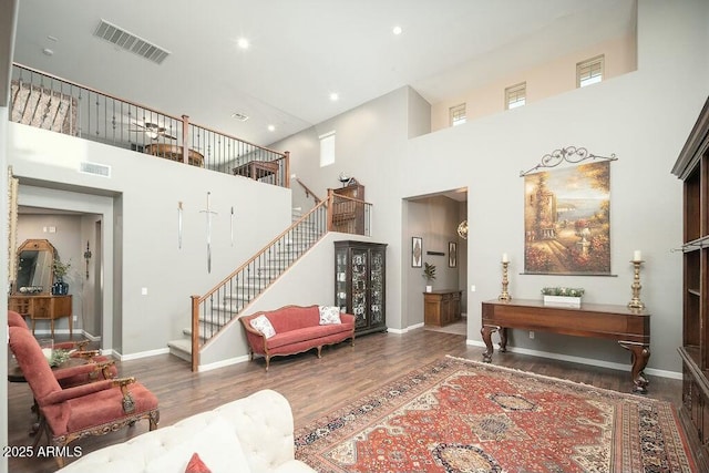 living room with stairway, wood finished floors, visible vents, baseboards, and a towering ceiling