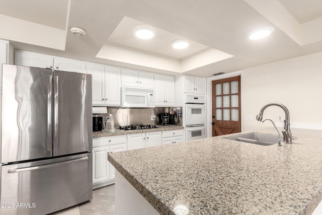 kitchen with white appliances, a raised ceiling, a sink, and white cabinets