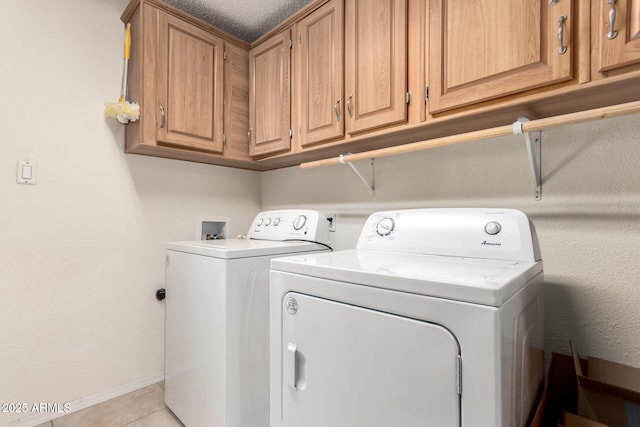 clothes washing area with light tile patterned floors, cabinet space, baseboards, and separate washer and dryer