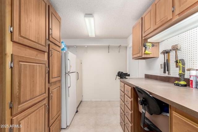 kitchen with freestanding refrigerator, brown cabinets, a textured ceiling, and light tile patterned floors