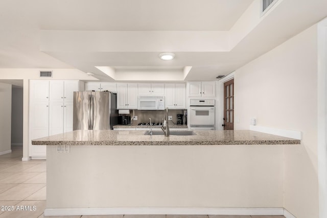 kitchen with light stone counters, white appliances, white cabinetry, visible vents, and a tray ceiling