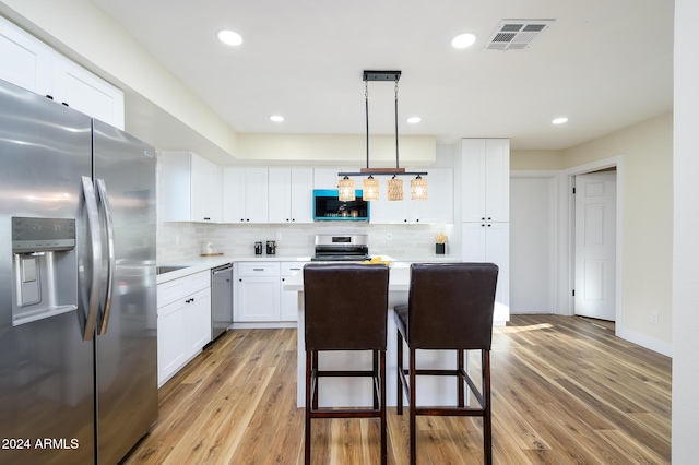 kitchen featuring white cabinets, decorative backsplash, light wood-type flooring, decorative light fixtures, and stainless steel appliances