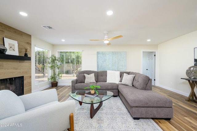 living room with a high end fireplace, hardwood / wood-style flooring, ceiling fan, and wood walls