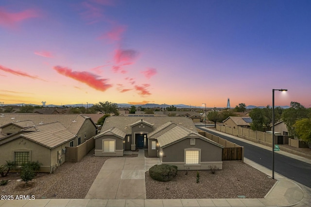 view of front of house with stucco siding, fence, a residential view, concrete driveway, and a tile roof