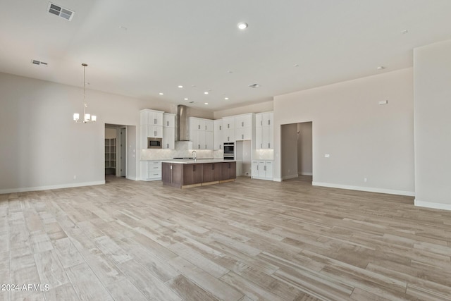 kitchen featuring appliances with stainless steel finishes, decorative light fixtures, white cabinetry, wall chimney range hood, and a spacious island