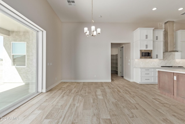 kitchen with pendant lighting, wall chimney range hood, stainless steel microwave, white cabinets, and decorative backsplash