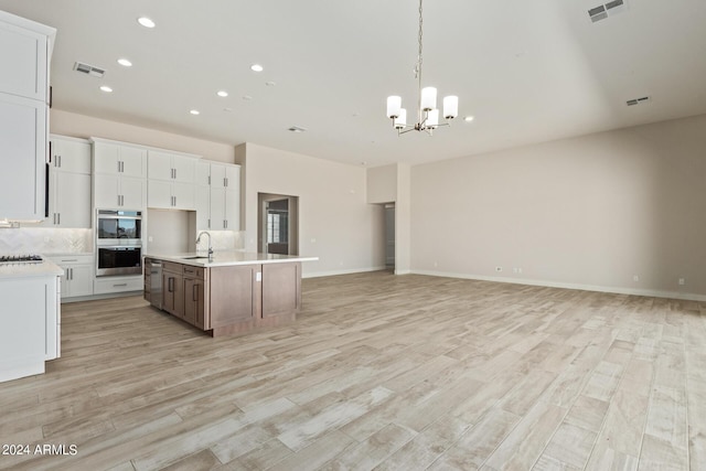 kitchen featuring sink, stainless steel appliances, tasteful backsplash, white cabinets, and a center island with sink