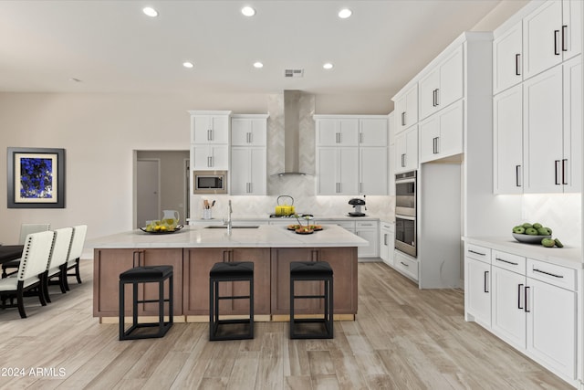 kitchen featuring a breakfast bar area, stainless steel appliances, wall chimney exhaust hood, and a sink