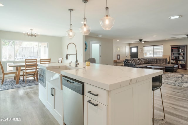 kitchen with dishwasher, light wood-type flooring, an island with sink, decorative light fixtures, and white cabinetry