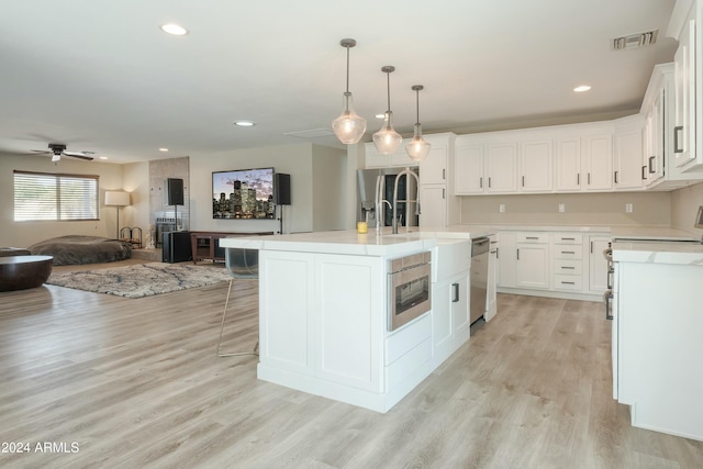 kitchen with white cabinets, ceiling fan, light wood-type flooring, and an island with sink