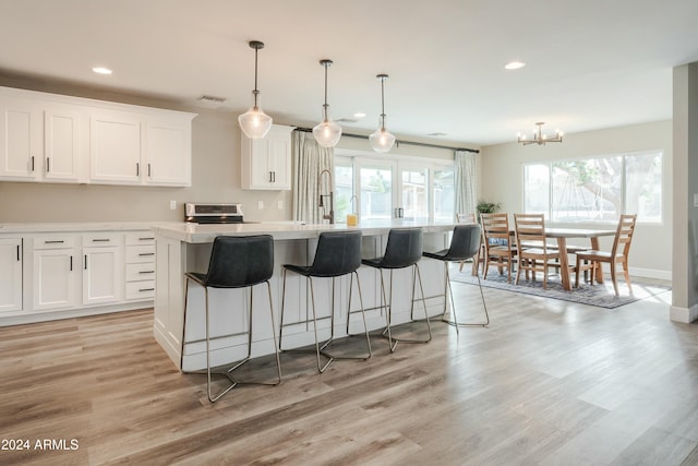 kitchen featuring a kitchen island with sink, decorative light fixtures, a notable chandelier, light hardwood / wood-style floors, and white cabinetry