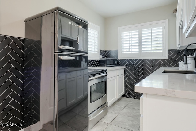 kitchen featuring white cabinets, black fridge, sink, light tile patterned floors, and stainless steel range oven