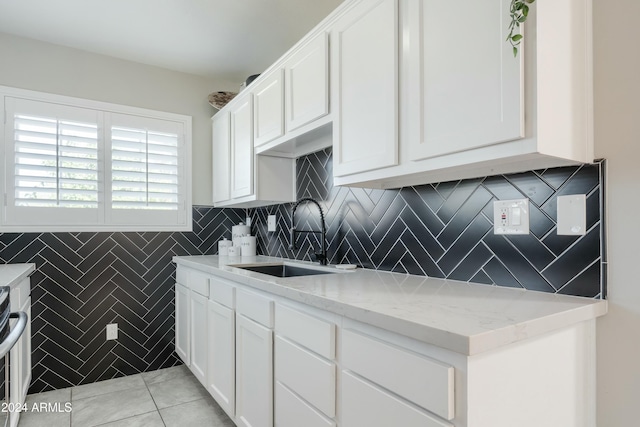 kitchen with white cabinets, light stone countertops, light tile patterned floors, and sink