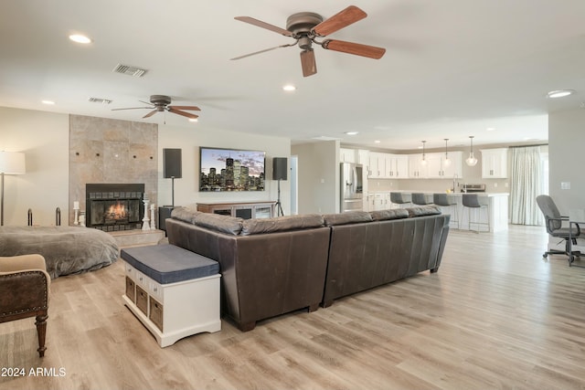 living room featuring a tile fireplace, light hardwood / wood-style flooring, and ceiling fan