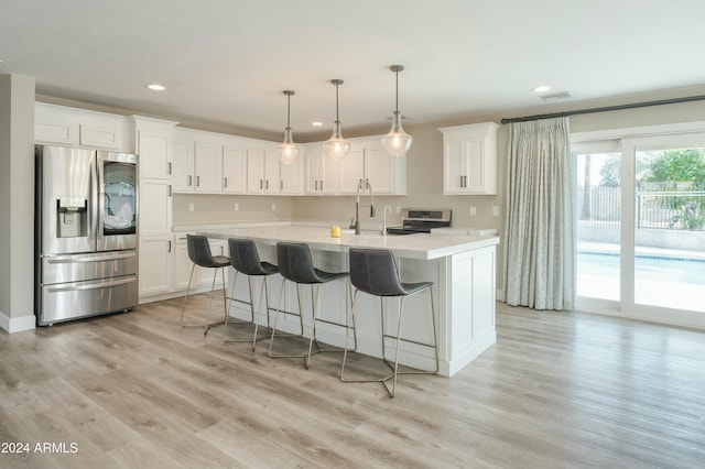 kitchen with hanging light fixtures, light hardwood / wood-style flooring, a center island with sink, white cabinets, and appliances with stainless steel finishes