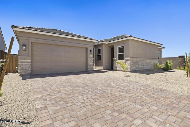 view of front of property featuring an attached garage, fence, stone siding, decorative driveway, and stucco siding