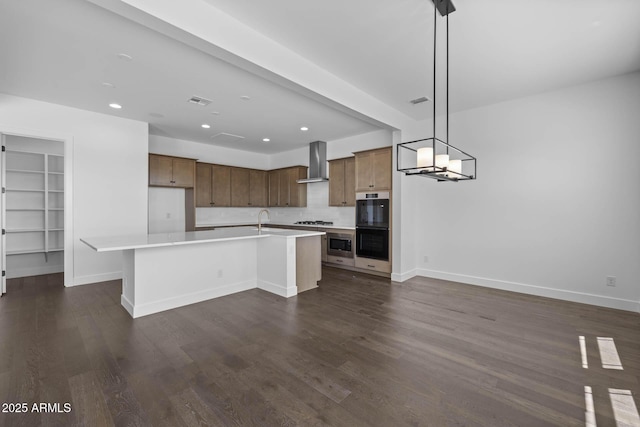 kitchen with wall chimney exhaust hood, dark wood finished floors, light countertops, and stainless steel gas stovetop