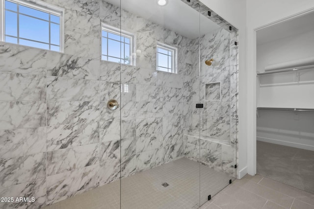 full bathroom featuring baseboards, a stall shower, a walk in closet, and tile patterned floors