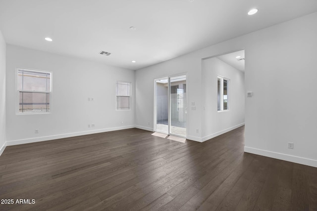 empty room featuring baseboards, plenty of natural light, visible vents, and dark wood-style flooring