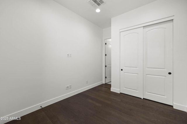 unfurnished bedroom with a closet, dark wood-style flooring, visible vents, and baseboards