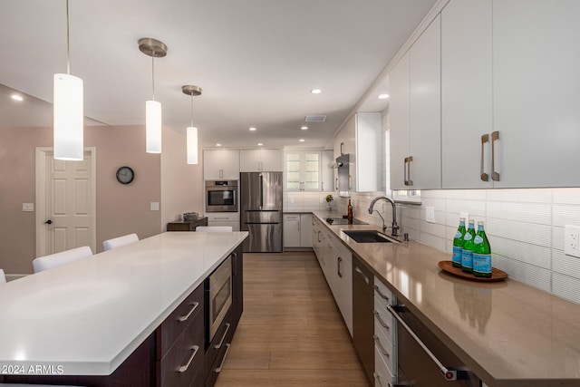 kitchen with hanging light fixtures, sink, a large island, light hardwood / wood-style flooring, and stainless steel appliances