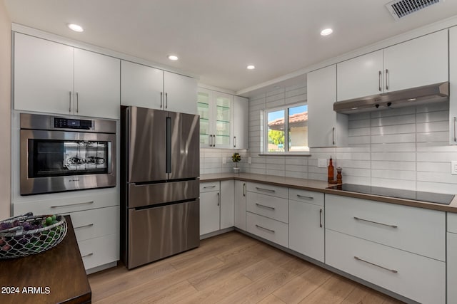 kitchen featuring white cabinets, backsplash, stainless steel appliances, and light wood-type flooring