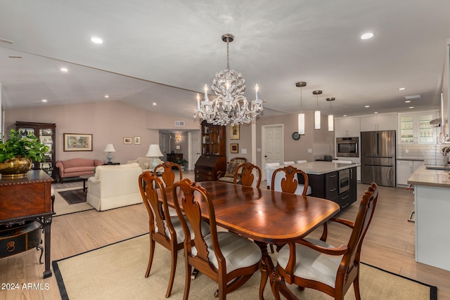 dining area with light wood-type flooring, vaulted ceiling, an inviting chandelier, and sink