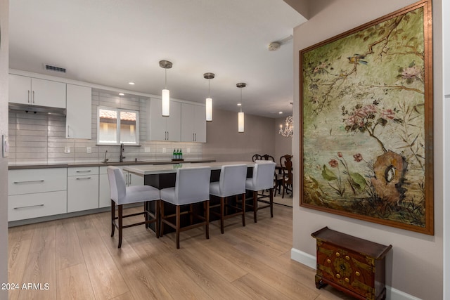 kitchen with a kitchen breakfast bar, light wood-type flooring, white cabinets, and hanging light fixtures