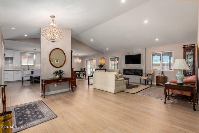 living room with a high end fireplace, a chandelier, vaulted ceiling, and light wood-type flooring