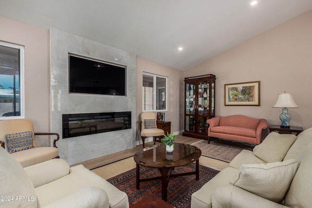 living room with a high end fireplace, vaulted ceiling, and hardwood / wood-style floors