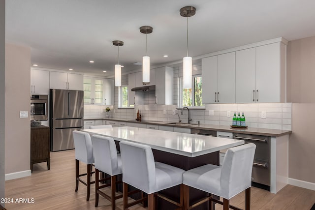 kitchen with hanging light fixtures, white cabinetry, stainless steel appliances, a center island, and light hardwood / wood-style flooring