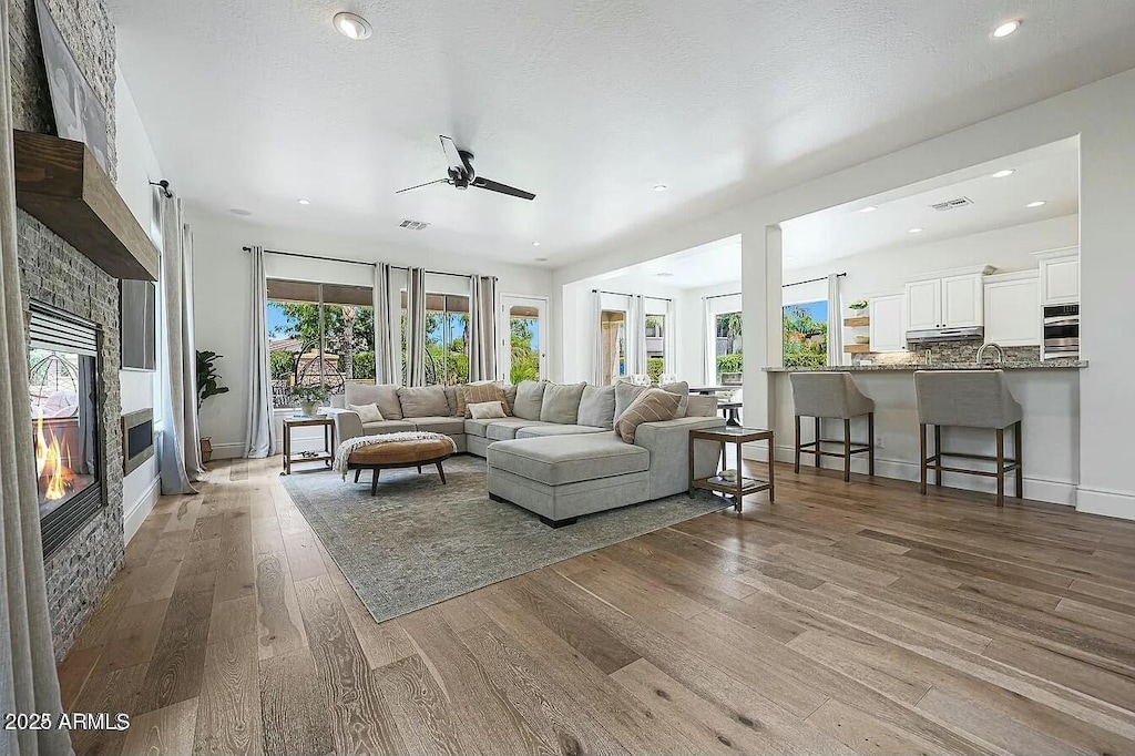 living room with a stone fireplace, hardwood / wood-style floors, sink, ceiling fan, and a textured ceiling