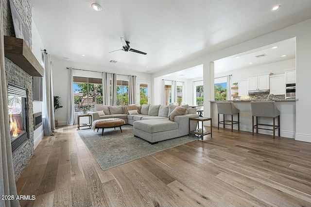 living room with a stone fireplace, hardwood / wood-style floors, sink, ceiling fan, and a textured ceiling