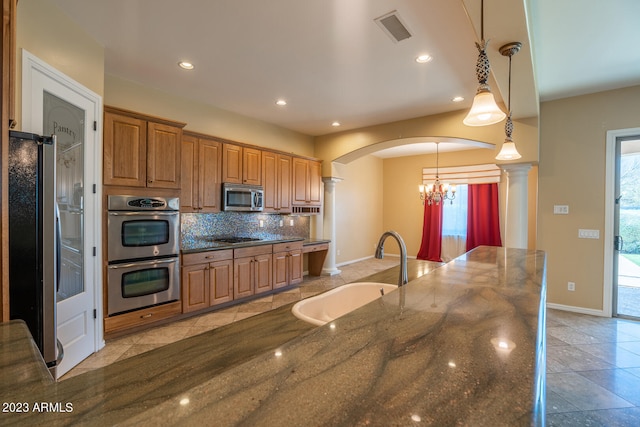 kitchen with backsplash, appliances with stainless steel finishes, sink, dark stone countertops, and a chandelier