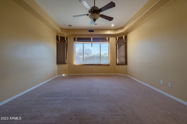 carpeted spare room featuring a raised ceiling and ceiling fan