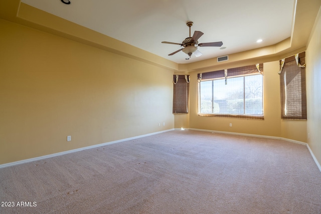 carpeted spare room featuring a raised ceiling and ceiling fan