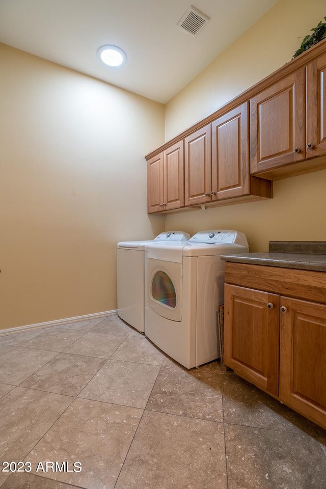 laundry area featuring washing machine and clothes dryer, cabinets, and light tile floors