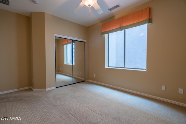 unfurnished bedroom featuring a closet, light carpet, multiple windows, and ceiling fan