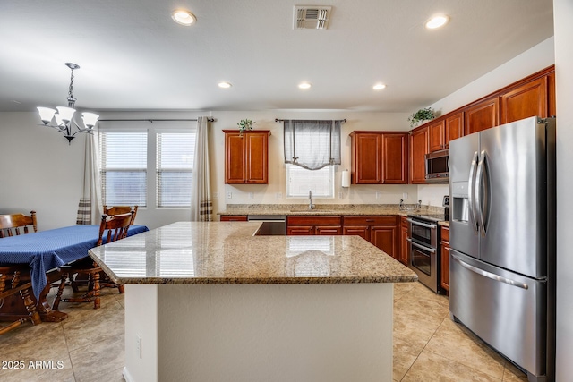 kitchen with light stone countertops, stainless steel appliances, a kitchen island, and pendant lighting