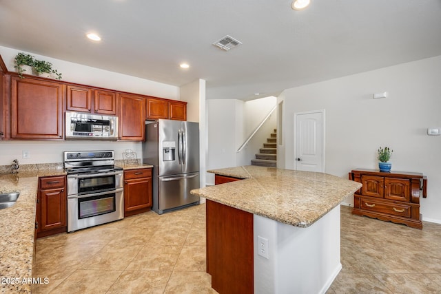 kitchen featuring stainless steel appliances, a kitchen island, light tile patterned floors, and light stone countertops