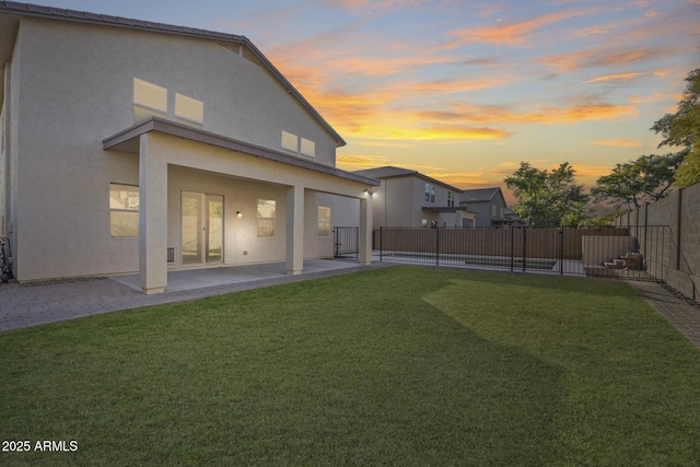 back house at dusk featuring a patio and a yard