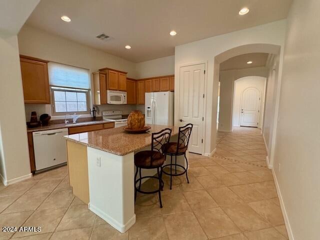 kitchen featuring light stone counters, sink, white appliances, a kitchen island, and a kitchen breakfast bar