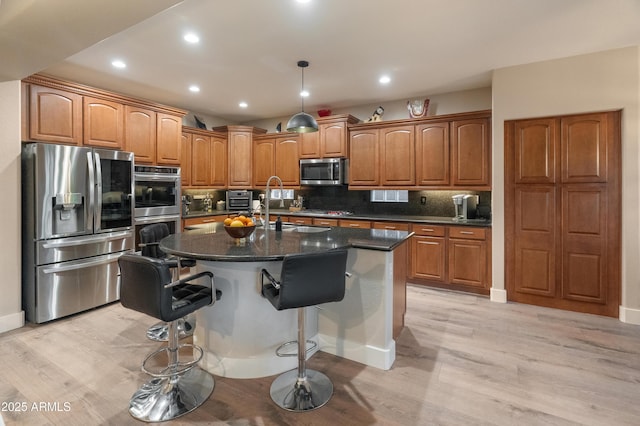 8447 W Tether Trl, Peoria, AZ 85383 - kitchen featuring appliances with stainless steel finishes, brown cabinets, a kitchen island with sink, light wood finished floors, and tasteful backsplash